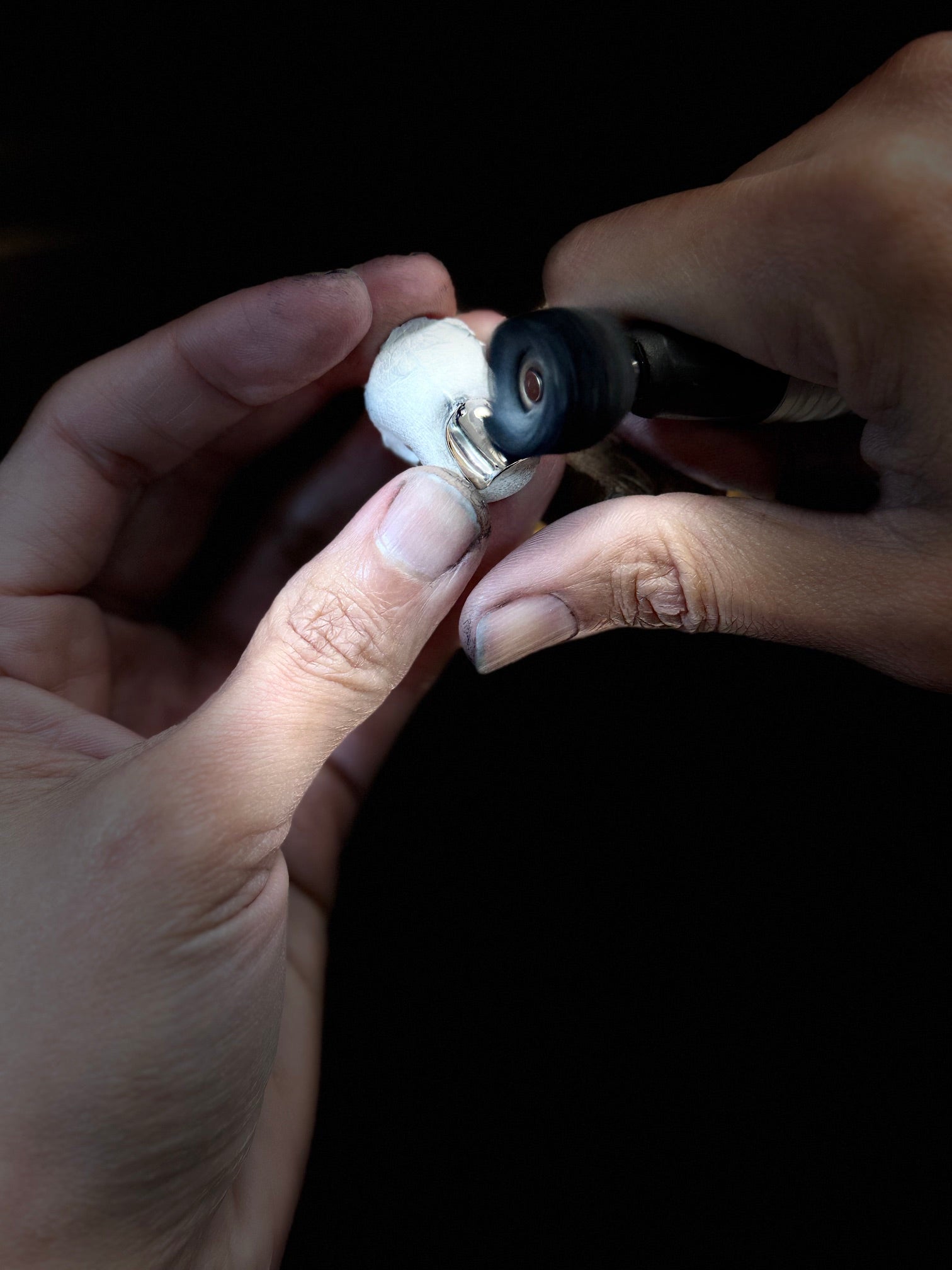 A close-up of a person's hands using a rotary diamond grinding tool to shape a small white object against a solid black background.