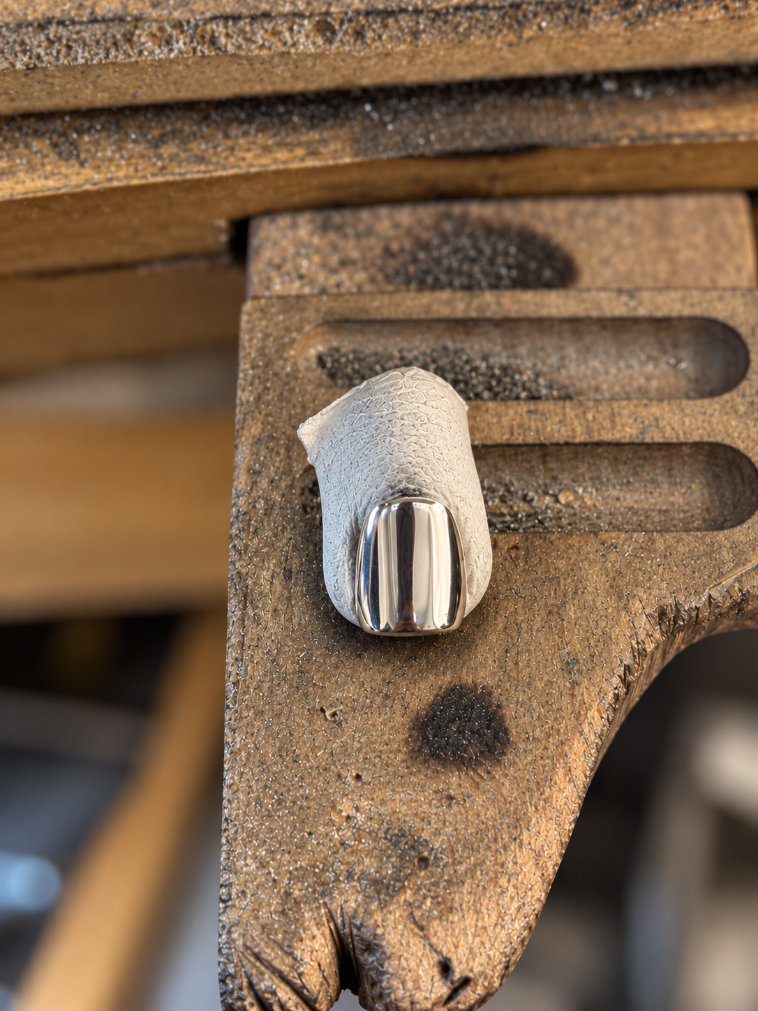A close-up of a polished silver metal nail head mounted on a textured, weathered brown metal surface.